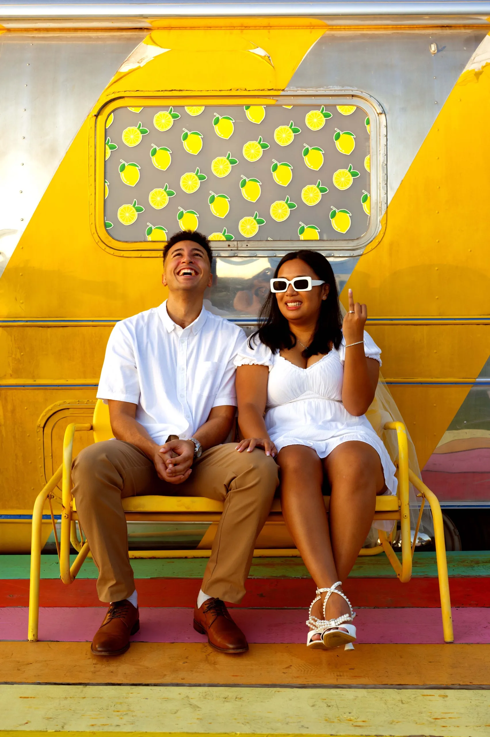The couple laughing on the yellow bench in front of the lemon trailer.