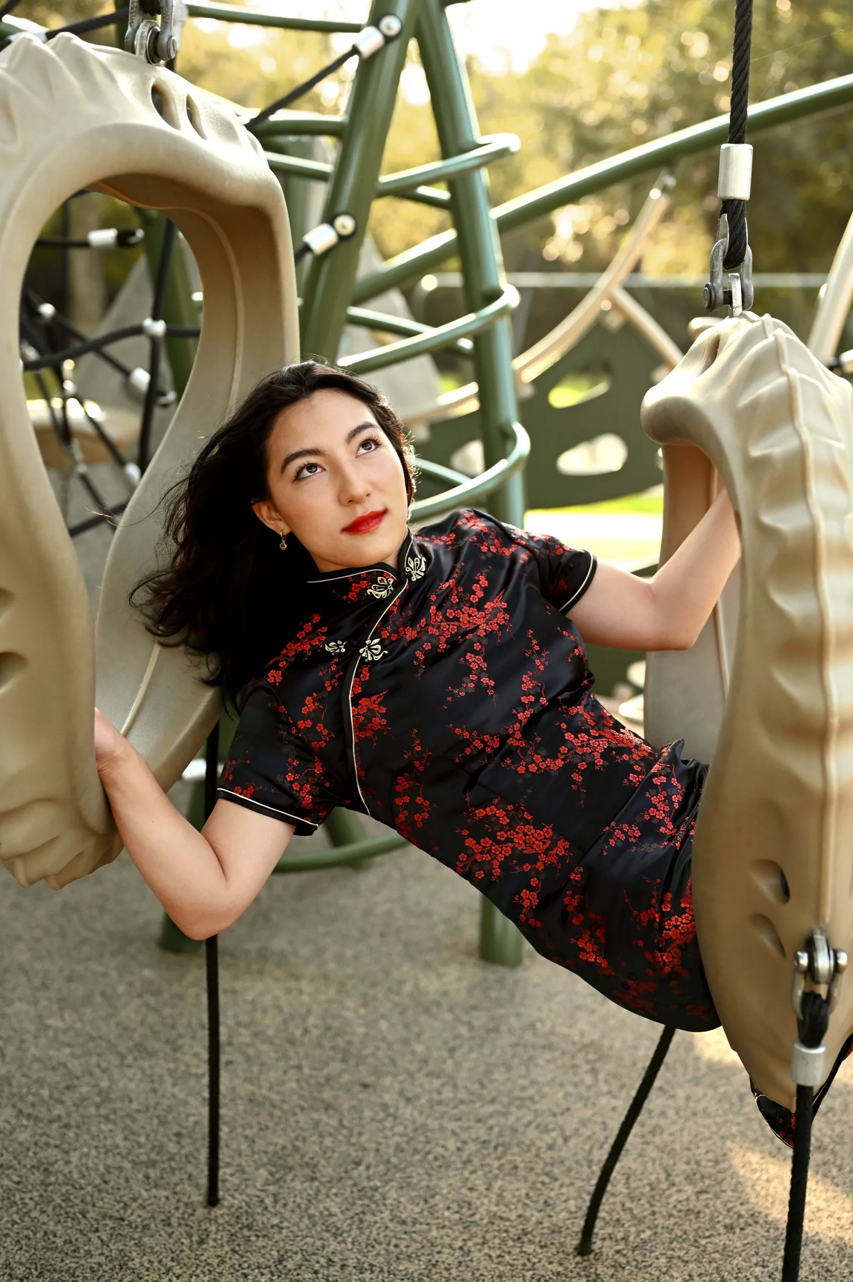 A woman in a red and black qipao lounging inside a curved playground climbing structure.
