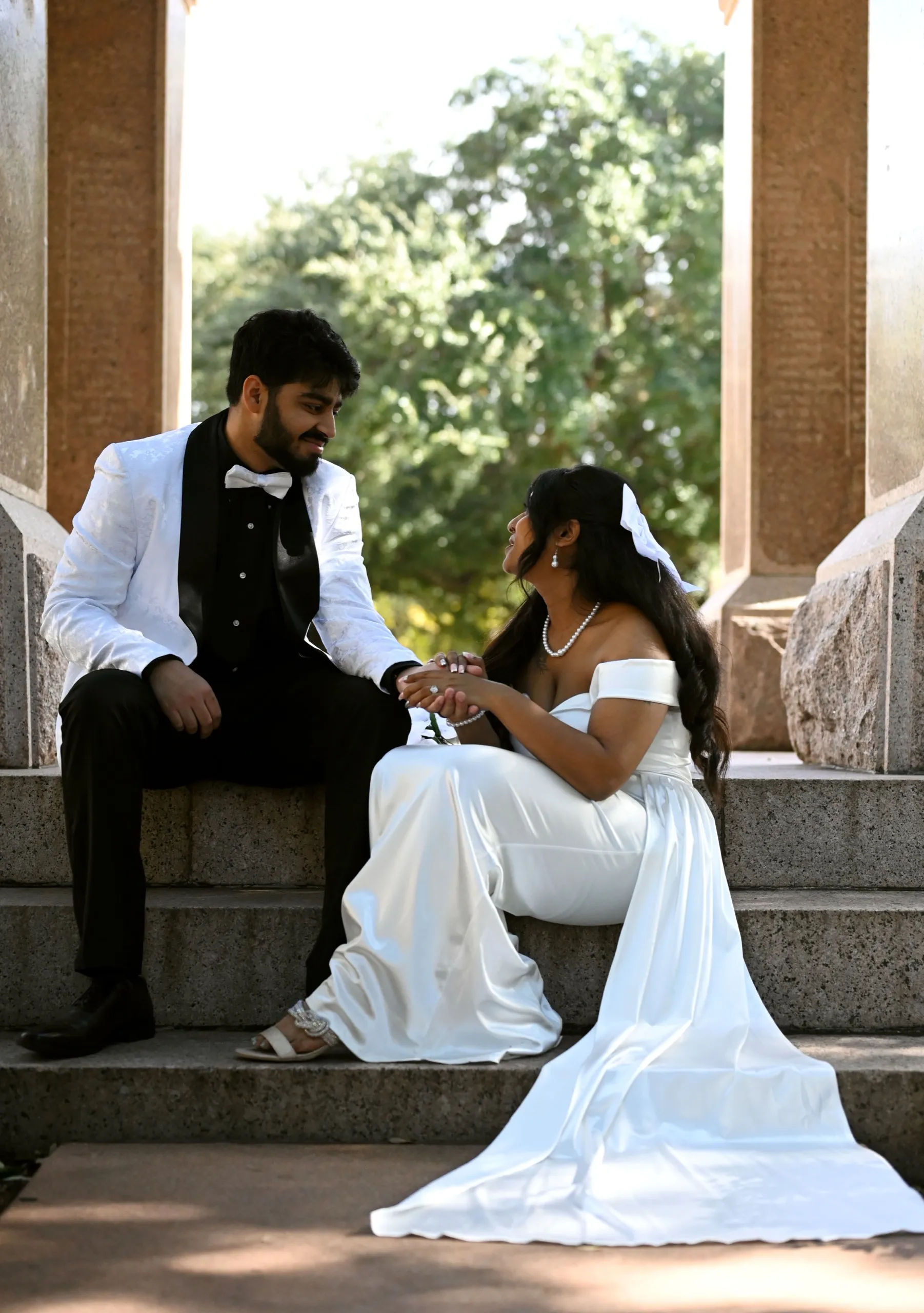 The couple holding hands on stone steps between tall columns, the bride's white gown spread across the steps.